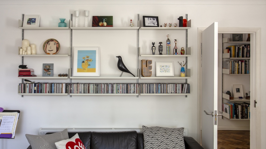 wall mounted shelving system, adjustable, modular 606 shelving for living room with CD, DVD media storage shelves, bookshelf in the background. Vitsœ 606, designer Dieter Rams