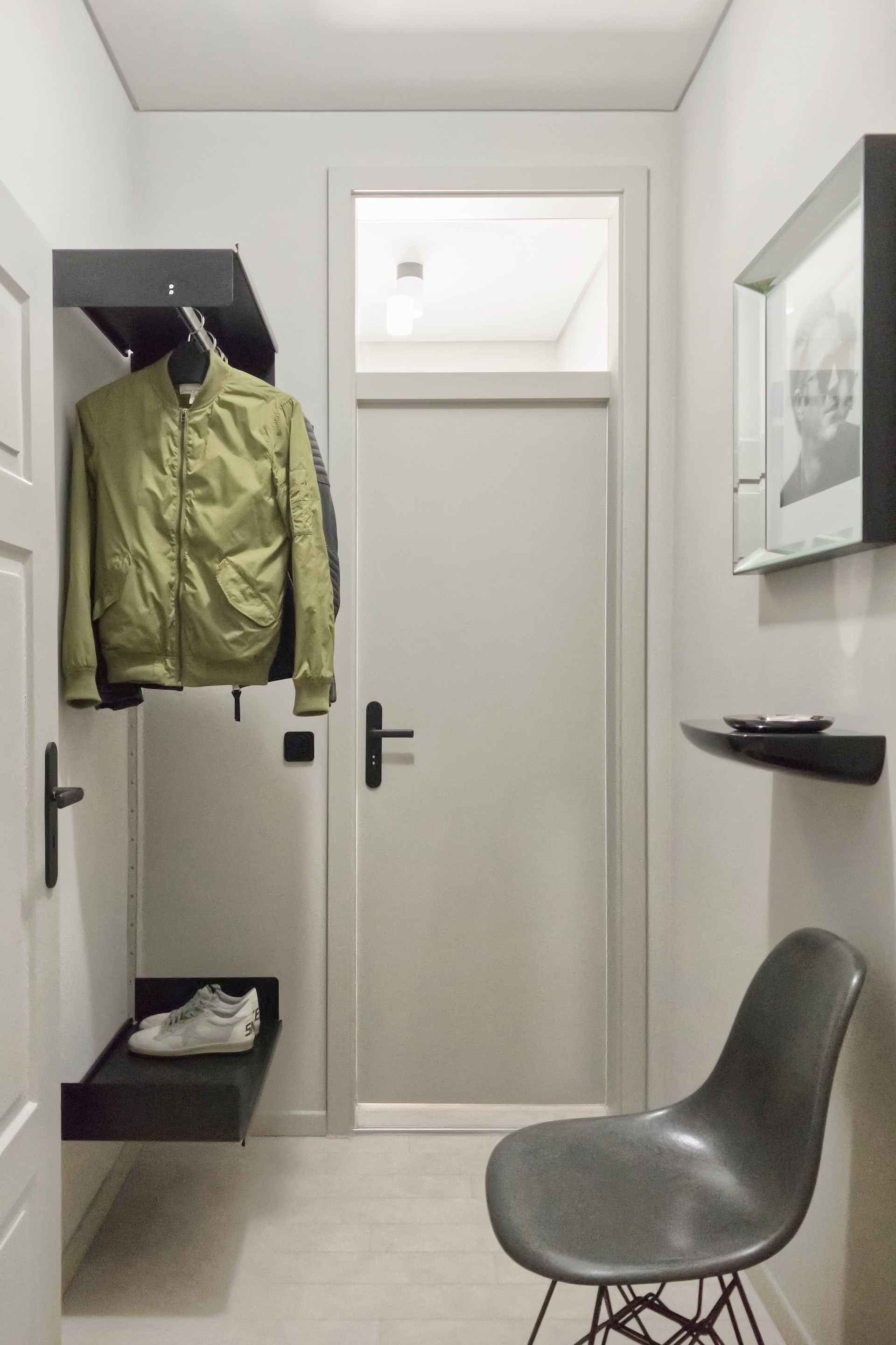 Custom made wall mounted shoe shelf in hallway. Clothes rail black designer shelves for hanging coats and storage. Strong metal. Vitsœ Modular 606 Shelving System. Design Dieter Rams.