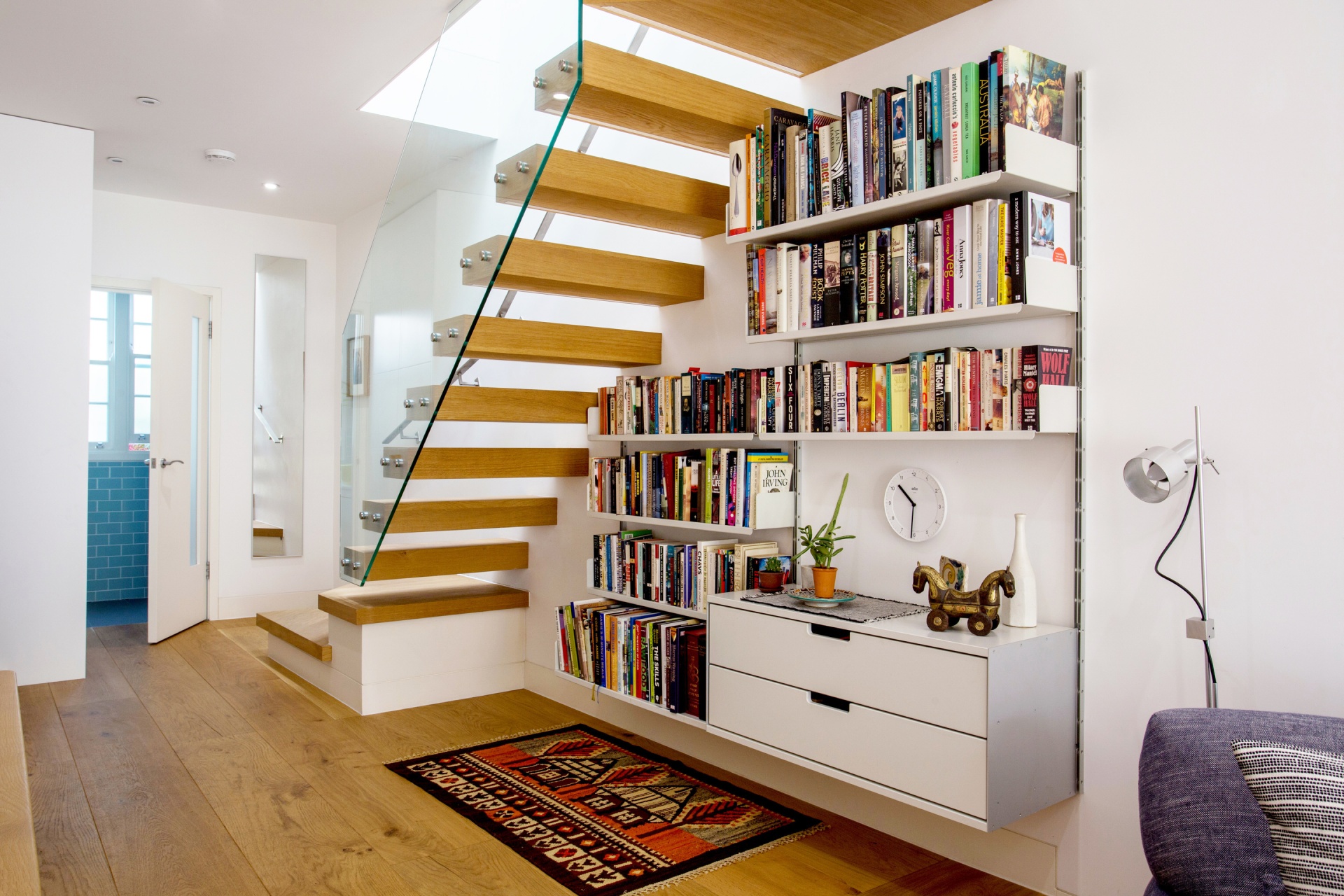 under stairs hallway modern bookshelves and floating sideboard cabinets. Vitsœ 606 modular shelving system. Wall mounted, off-white. Designer Dieter Rams, Vitsœ.