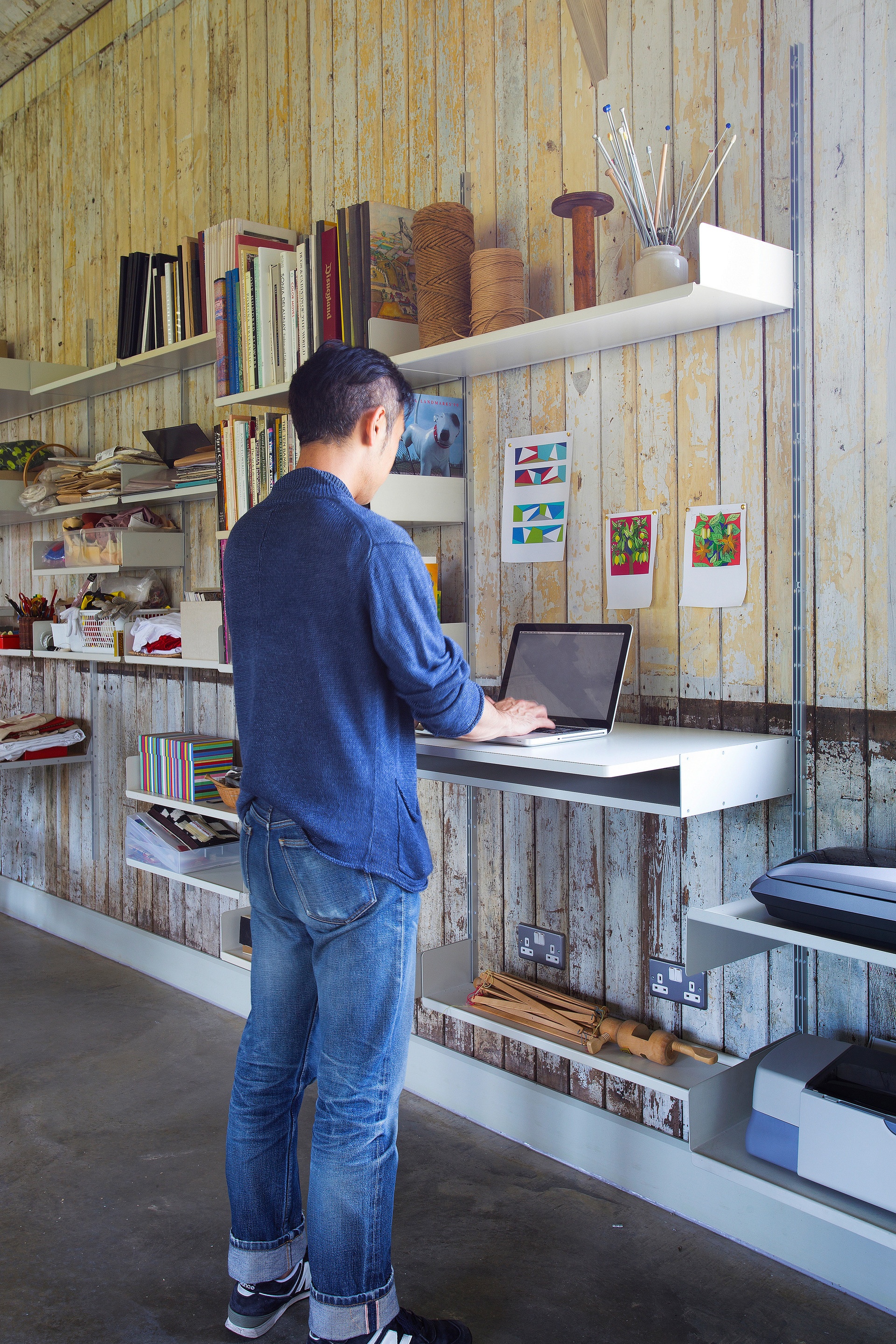 Modular shelving system with standing desk and strong shelves for printer and scanner, box file storage. Above desk shelving unit in off-white, wall-mounted bookshelves, modern home office for creative studio. Designer shelves, Dieter Rams. Vitsœ 606 Universal Shelving System.