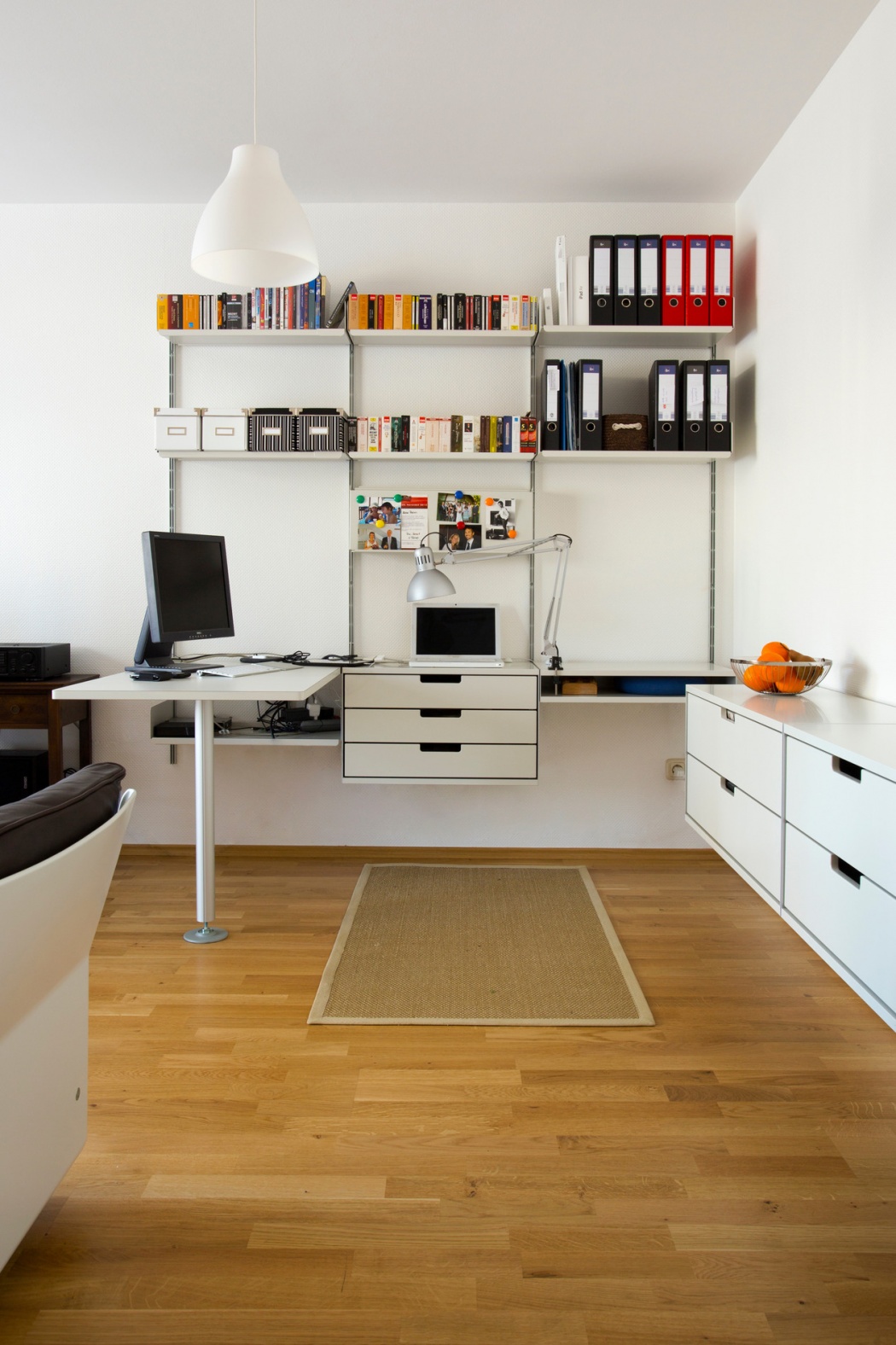 Modular shelving system with integrated table desk and strong shelves for book collection and box file storage. Above desk shelving unit in off-white, wall-mounted bookshelves for modern home office in the living room. Sideboard drawer cabinets, and 620 armchair in black leather. Designer shelves, Dieter Rams. Vitsœ 606 Universal Shelving System.